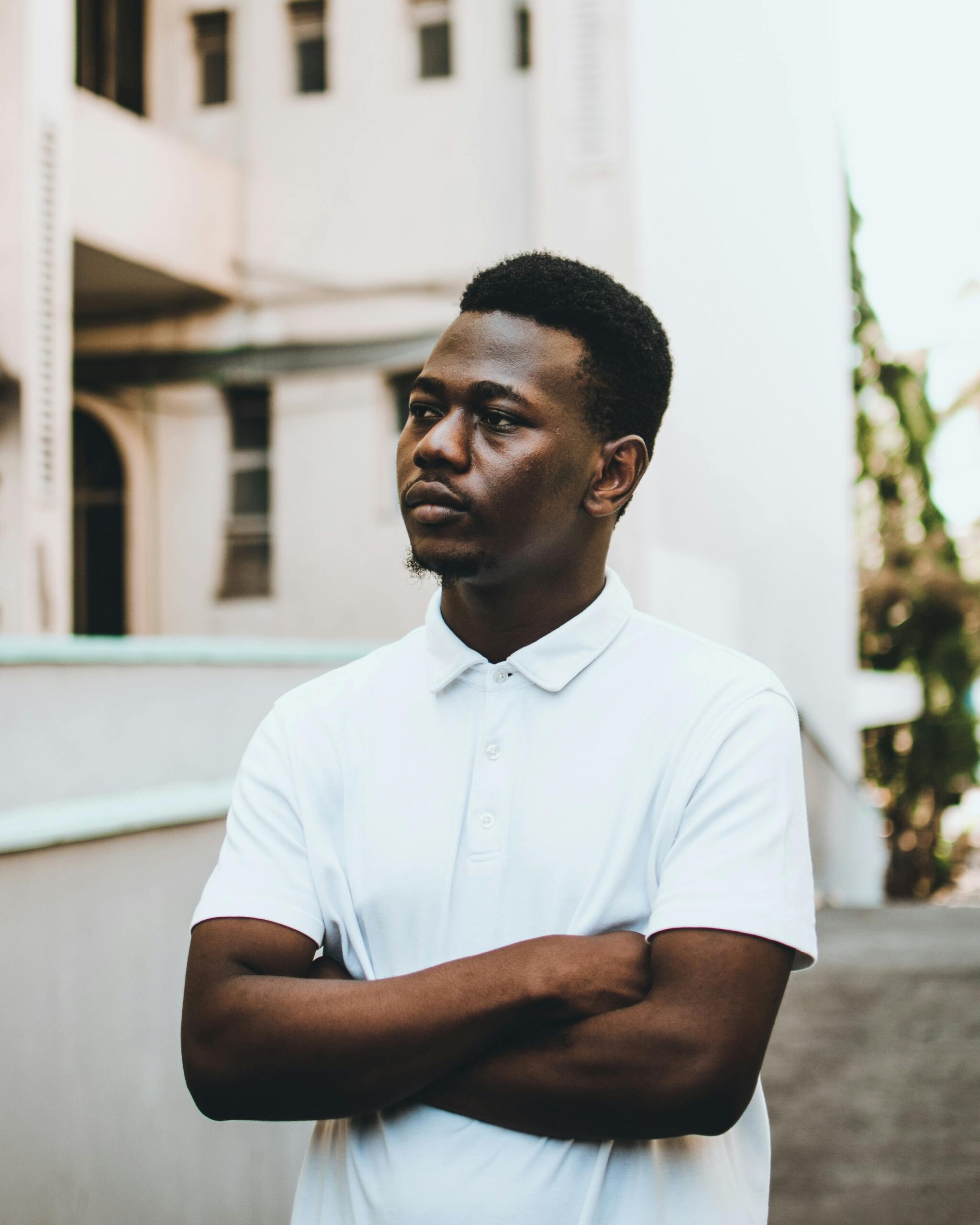 A young man poses seriously in a white polo shirt outdoors against a neutral background.