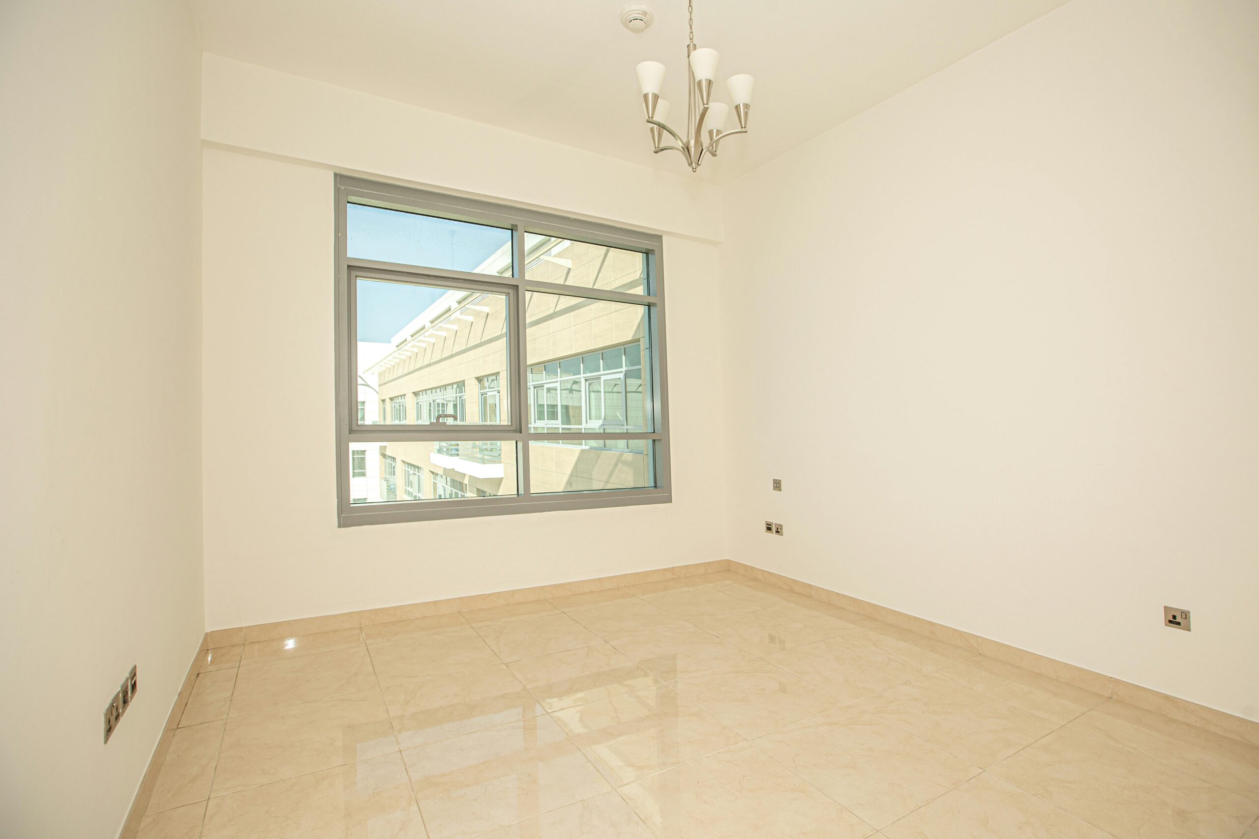 Spacious empty room with large window and chandelier, showcasing minimalistic design.