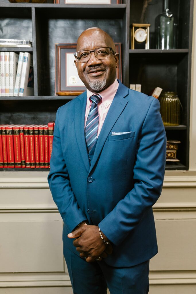Middle-aged man in a blue suit smiling confidently in an elegant office environment.